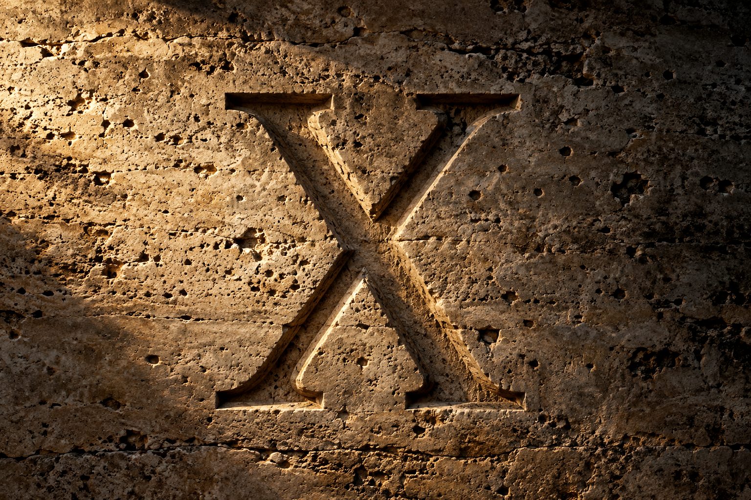 A Roman numeral X chiselled into travertine, grazed by golden light